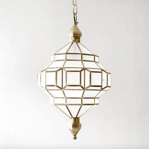 Puede incluir: Una lámpara colgante geométrica blanca con un marco de metal dorado. La lámpara tiene una parte superior e inferior puntiagudas y está suspendida de una cadena.