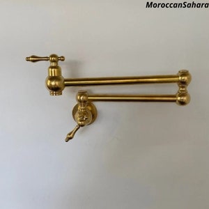 May include: A gold-toned kitchen faucet with a swivel spout and two handles. The faucet is mounted on a wall.