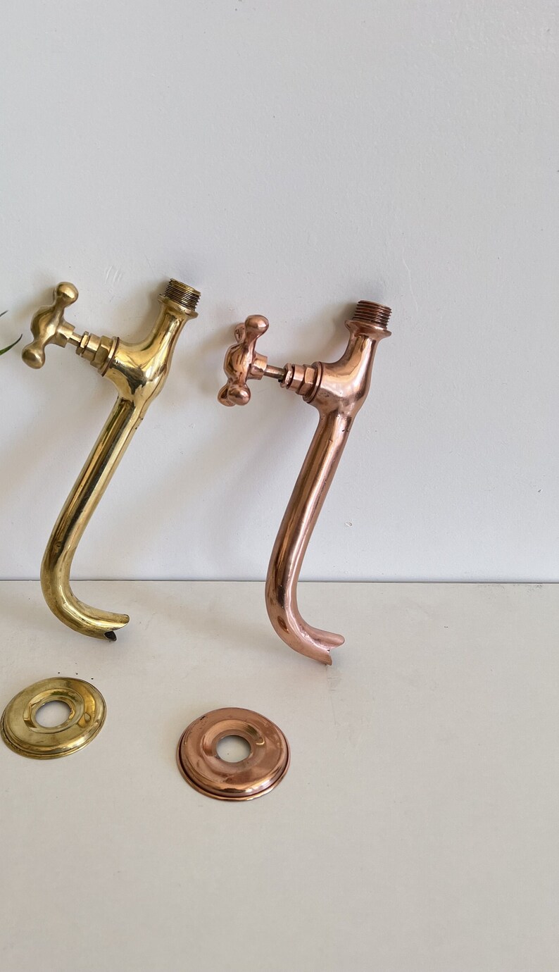 Puede incluir: Dos grifos de estilo antiguo, uno dorado y otro de cobre, con rosetas redondas a juego. Los grifos tienen un dise&ntilde;o tradicional con una manija en forma de cruz.