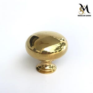 May include: A polished gold cabinet knob with a rounded top and a short, cylindrical base.
