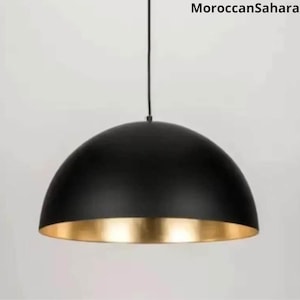 May include: Black dome pendant light with a gold interior. The light fixture is suspended from a black cord.