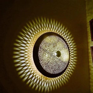 May include: A round, decorative ceiling light fixture with a intricate, geometric pattern. The light casts a shadow on the wall behind it, creating a similar pattern.