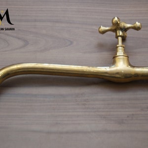 Puede incluir: Un grifo de latón con un caño largo y curvo y una manija en forma de cruz. El grifo está sobre una superficie de madera.