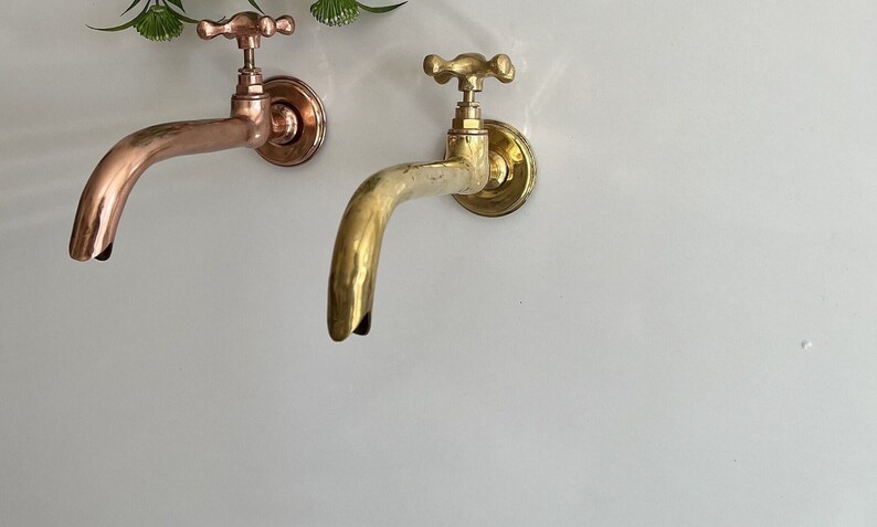 Puede incluir: Dos grifos de pared de estilo antiguo, uno de cobre y otro de lat&oacute;n, con manijas en forma de cruz.
