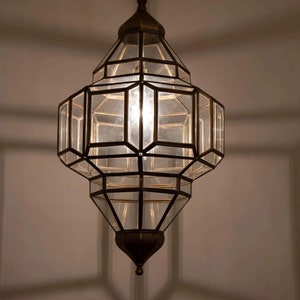 May include: A brass and glass pendant light with a geometric design. The light is hanging from a chain and has a clear glass shade.