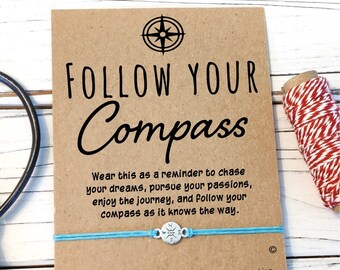 May include: A blue and silver compass charm bracelet with a brown card that reads "Follow Your Compass". The card also includes the text "Wear this as a reminder to chase your dreams, pursue your passions, enjoy the journey, and follow your compass as it knows the way."  The card also includes the text "Close your eyes, tie this string and make a wish, when the string breaks in two, it's believed that your wish will become true! Dream it, believe, it will happen! (TM)"