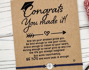 May include: A graduation card with a blue string bracelet and a compass charm. The card has a message that says "Congrats You Made It!" and includes a quote about following your dreams.