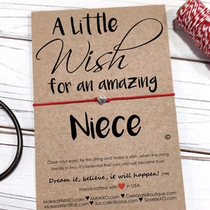 May include: A red string bracelet with a silver heart charm on a brown card with the text "A Little Wish for an amazing Niece". The card also includes instructions on how to make a wish and the text "Dream it, believe, it will happen!"