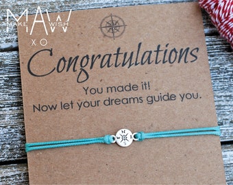 May include: A brown card with the text "Congratulations You made it! Now let your dreams guide you."  A teal blue string bracelet with a silver compass charm is on the card. The card has a recycle symbol and the text "If you would like to swap the card with one of our standard MAWXO cards at no extra charge, simply leave a message in the note to seller section at checkout."