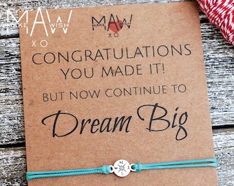 May include: A kraft paper card with the text "MAW Congratulations You Made It! But Now Continue To Dream Big" and a turquoise bracelet with a compass charm. The card is recyclable.