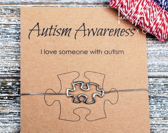 May include: A brown card with the text "Autism Awareness" and "I love someone with autism". A silver puzzle piece charm bracelet is on the card. The text on the card continues, "and I wear this bracelet as a reminder of the joy they bring to my life."