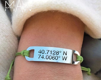 May include: A green cord bracelet with a silver tag that reads "40.7128° N 74.0060° W".
