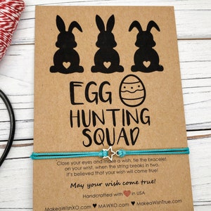 May include: A brown card with three black bunny silhouettes and an Easter egg design. The card says "Egg Hunting Squad". A turquoise string bracelet with a silver star charm is attached to the card. The card also says "Close your eyes and make a wish, tie the bracelet on your wrist, when the string breaks in two, it's believed that your wish will come true! May your wish come true! Handcrafted with in USA MakeaWishXO.com MAWXO.com MakeaWishTrue.com"
