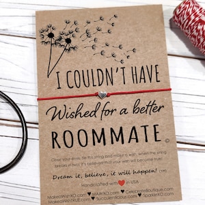 May include: Red string bracelet with a silver heart charm and a card that reads "I couldn't have wished for a better roommate." The card has a dandelion design and the text "Dream it, believe, it will happen!"