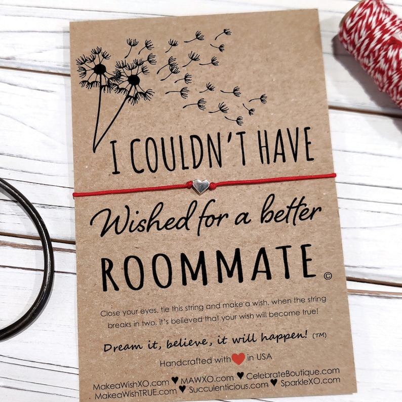 May include: Red string bracelet with a silver heart charm and a card that reads "I couldn't have wished for a better roommate." The card has a dandelion design and the text "Dream it, believe, it will happen!"