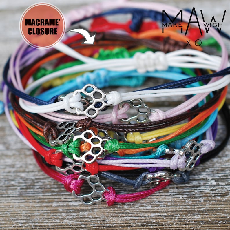 Puede incluir: Una pila de pulseras de colores con cierres de macram&eacute; y dijes de metal plateado. Las pulseras est&aacute;n hechas de cord&oacute;n delgado y est&aacute;n dispuestas en un patr&oacute;n de arco&iacute;ris.