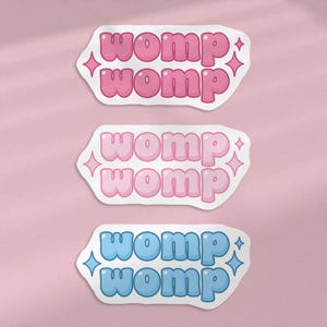 Può includere: Tre adesivi con la parola "womp" ripetuta due volte su ciascuno. L'adesivo superiore è rosa, l'adesivo centrale è rosa chiaro e l'adesivo inferiore è blu.