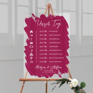Könnte beinhalten: Ein rosa-weißes Hochzeitsschild mit einem Pinselstrich-Design. Das Schild listet die Ereignisse des Hochzeitstages mit Uhrzeiten auf, darunter die Trauung, der Empfang und die Party. Der Text lautet "Unser Tag" und "Marjan & Steffen" mit dem Datum "19.05.2018" und "Schloss Hammerstein".
