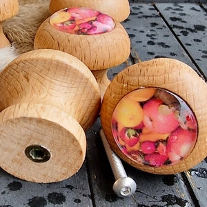 Könnte beinhalten: Holzknauf für Schränke mit rundem, buntem Blumendesign. Die Knäufe sind hellbraun und haben eine silberne Schraube.
