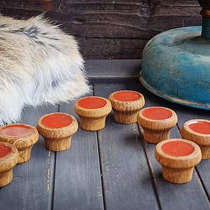 Könnte beinhalten: Acht Holzknöpfe mit einem rot-orangen Oberteil, angeordnet auf einer dunkelgrauen Holzoberfläche. Die Knöpfe haben ein strukturiertes, geschnitztes Design. Eine blaue und goldene Vintage-Lampe und ein Kunstfellteppich befinden sich im Hintergrund.