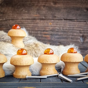 Könnte beinhalten: Eine Sammlung von Holzschrankknöpfen mit bernsteinfarbenen Glasaufsätzen. Die Knöpfe sind pilzförmig und liegen auf einer dunklen Oberfläche mit silbernen Schrauben. Der Hintergrund zeigt eine Holzwand und ein fellartiges Material.