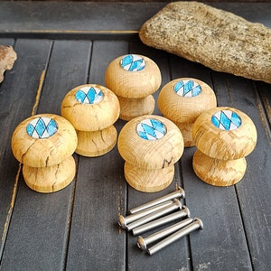 Könnte beinhalten: Sechs Holzknaufgriffe mit blauen und weißen Diamantenmuster-Einlagen. Die Griffe sind rund und haben einen leicht erhöhten Rand um die Einlage.
