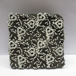 May include: A black wooden printing block with a white design of repeating hearts and floral patterns.