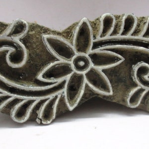 Könnte beinhalten: Ein Holzblock-Stempel mit einem floralen Design. Das Design zeigt eine Blume mit fünf Blütenblättern und einem Wirbelmuster.