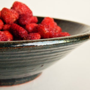 May include: A dark green ceramic bowl filled with fresh red strawberries. The bowl has a slightly rippled surface and a wide rim.