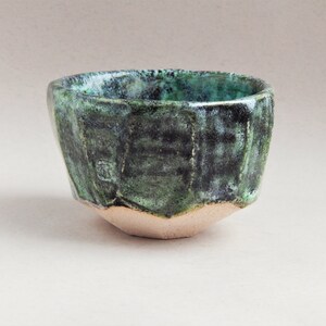 May include: A small, green ceramic bowl with a geometric shape. The bowl has a textured, speckled glaze.