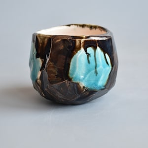 May include: A small, dark brown ceramic bowl with a textured, rocky exterior. The bowl has a light blue glaze with a crackled finish, creating a unique and artistic look.