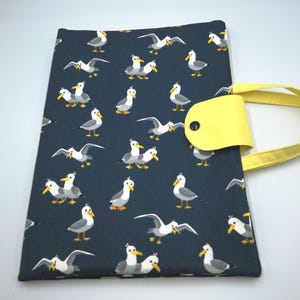 Può includere: Una borsa tote blu navy con un motivo di gabbiani bianchi e grigi con becchi gialli. La borsa ha un manico giallo e una patta gialla con chiusura a bottone nero. La borsa è in tessuto.