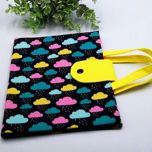 Puede incluir: Una bolsa de tela negra con asa amarilla y cierre de botón amarillo. La bolsa tiene un estampado colorido de nubes y gotas de lluvia.