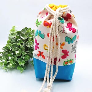 May include: A white drawstring bag with a blue bottom. The bag is decorated with colorful butterflies. The bag has a white drawstring.