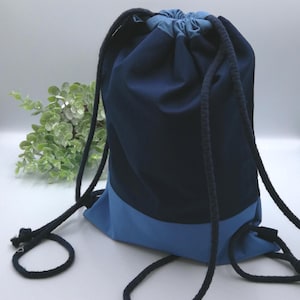 Pode incluir: Uma bolsa de cordão azul com a parte superior azul escura e a inferior azul clara. A bolsa tem um cordão longo azul escuro.