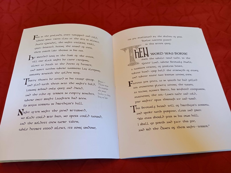 Puede incluir: Libro abierto con texto impreso en una fuente estilizada. Las letras iniciales son decorativas. El libro est&aacute; sobre una superficie roja. El texto parece ser un poema o una obra literaria.