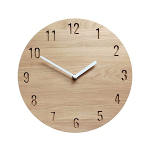 May include: A round wooden clock with white hands and black numbers. The clock face is made of light wood with a grain pattern. The numbers are carved into the wood and are easy to read.