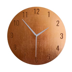 Peut inclure: Une horloge ronde de couleur cuivre avec des aiguilles blanches et des chiffres romains noirs. Le cadran de l'horloge a une texture en bois.