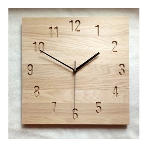 Può includere: Un orologio quadrato in legno con lancette nere e numeri romani. Il quadrante dell'orologio è in legno chiaro con una venatura.