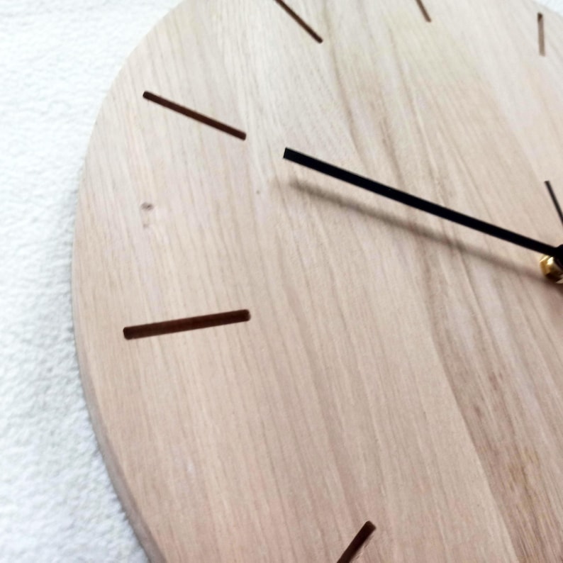 May include: A close-up of a wooden wall clock. The clock face is made of light-colored wood with dark brown markings for the hours. The clock hands are black, and the second hand is visible.