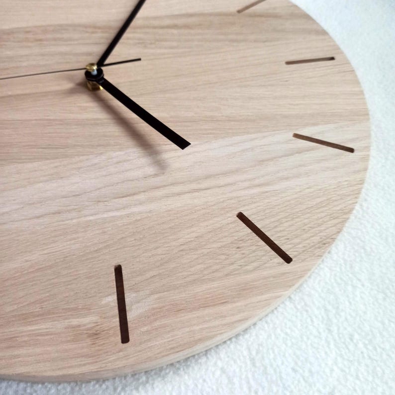 May include: A close-up of a round wooden clock with a light wood grain finish. The clock has black hands and simple brown line markers for the hours. The clock's hands are positioned to show the time.