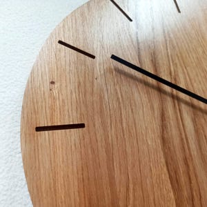 以下が含まれることがあります： 木製の時計の文字盤のクローズアップ。自然な木目があります。時計は黒い針とシンプルな線形の時間マーカーを備えています。デザインはミニマリストでモダンで、家の装飾に適しています。
