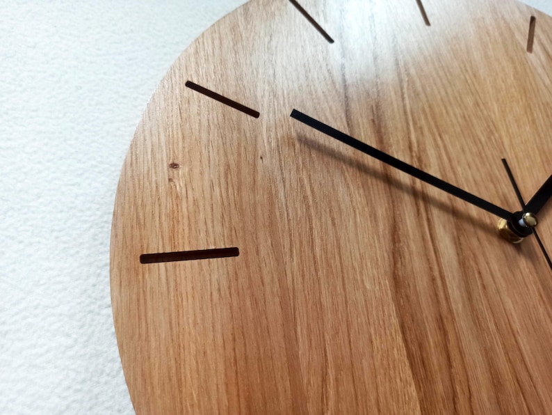 以下が含まれることがあります： 木製の時計の文字盤のクローズアップ。自然な木目があります。時計は黒い針とシンプルな線形の時間マーカーを備えています。デザインはミニマリストでモダンで、家の装飾に適しています。