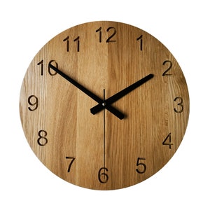 Könnte beinhalten: Eine runde Holzuhr mit schwarzen Zeigern und römischen Ziffern. Das Zifferblatt der Uhr ist aus hellbraunem Holz mit einer Maserung.