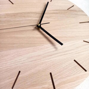 May include: A close-up of a wooden clock face with black hands and hour markers. The clock has a light wood grain finish. The hands are positioned to show the time. The clock is a decorative item.