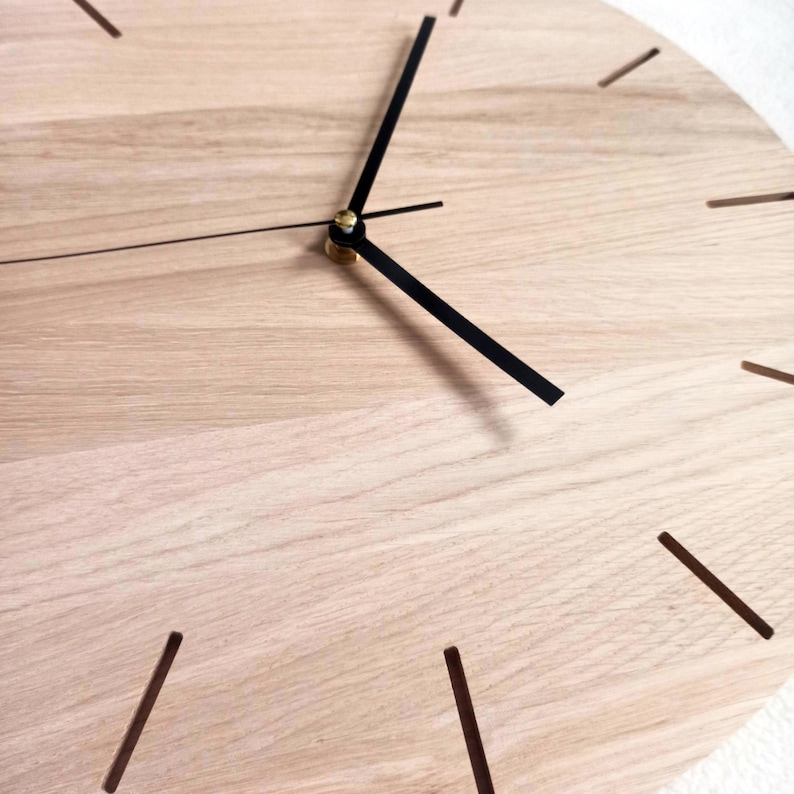 May include: A close-up of a wooden clock face with black hands and hour markers. The clock has a light wood grain finish. The hands are positioned to show the time. The clock is a decorative item.
