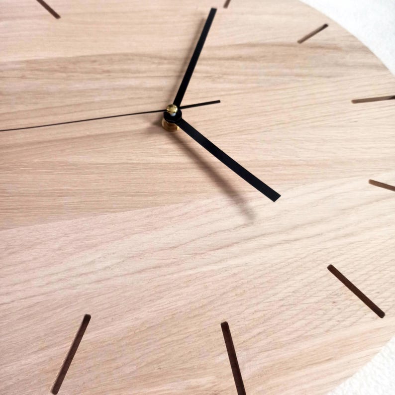 May include: A close-up of a wooden clock face with black hands and hour markers. The clock has a light wood grain finish. The hands are positioned to show the time. The clock is a decorative item.
