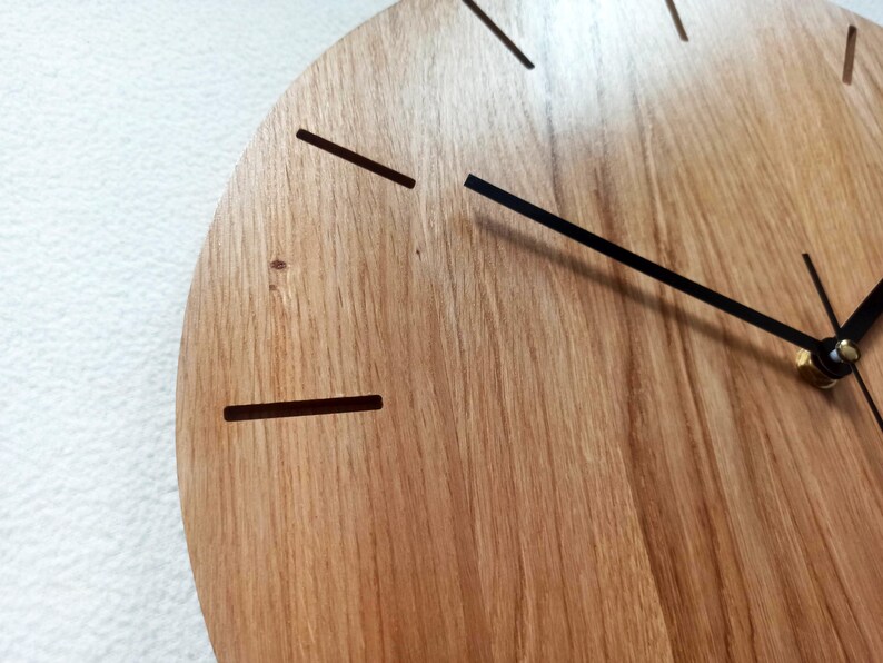 以下が含まれることがあります： 天然木目の木製時計の文字盤のクローズアップ。時計は黒い針とシンプルな線形の時間マーカーを備えています。デザインはミニマリストでモダンで、インテリアに適しています。