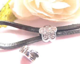 May include: A silver charm with a flower design and clear rhinestones, attached to a black leather cord.