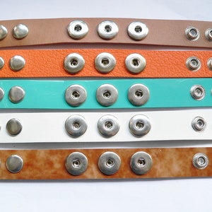Könnte beinhalten: Fünf Lederarmbänder mit Druckknöpfen. Die Armbänder sind in Braun, Orange, Türkis, Weiß und Braun mit Marmormuster. Die Druckknöpfe sind silberfarben.